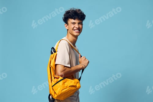 Preview: Young man smiling with a yellow backpack against a blue background, vibrant and cheerful concept