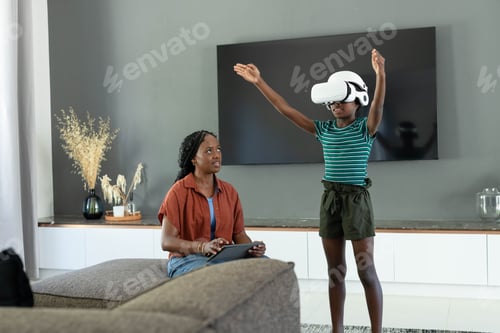 Preview: African American mother and child playing in living room with VR headset and tablet