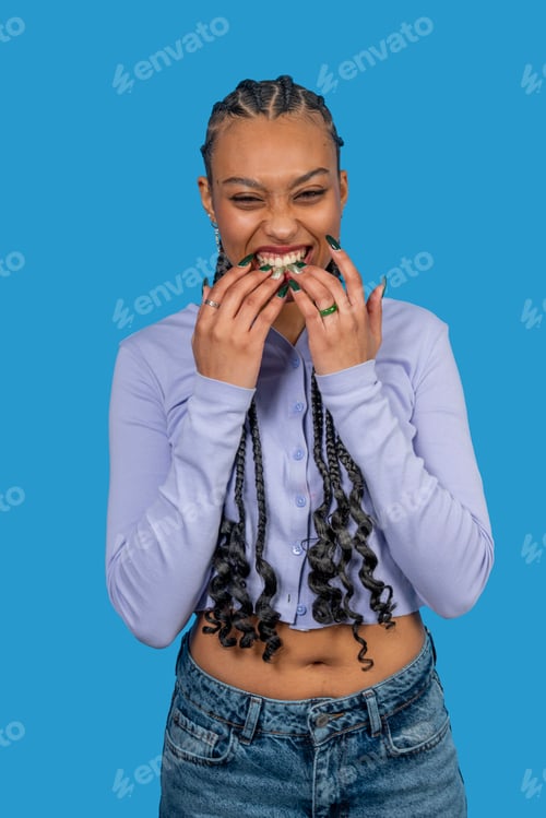 Preview: Young woman biting her nails and laughing on blue background