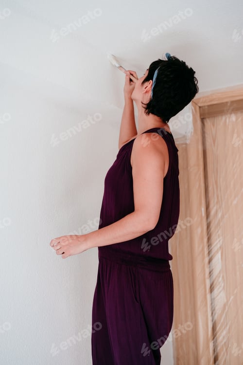 Preview: caucasian woman painting the room walls with white color. Do it yourself and new home concept