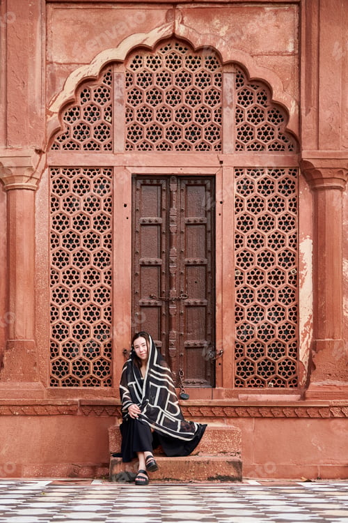 Preview: East asian woman in black dress sitting on steps of entrance to indian temple