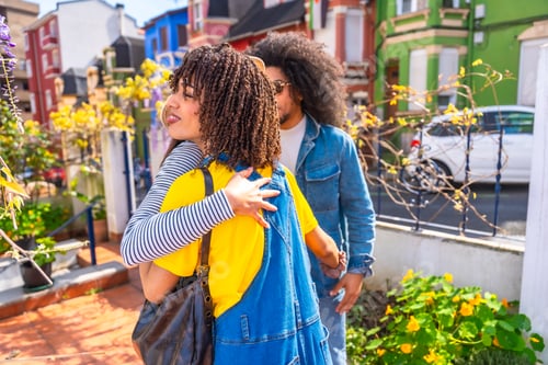 Preview: Two friends hugging in front of their colorful houses