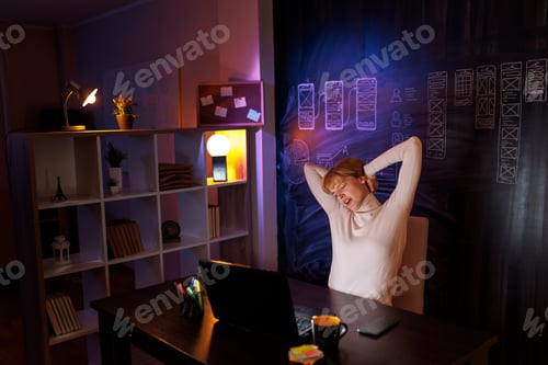 Preview: Woman stretching out at her desk while working overtime