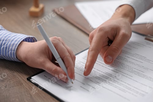 Preview: Notary pointing at document and client putting signature at wooden table indoors, closeup