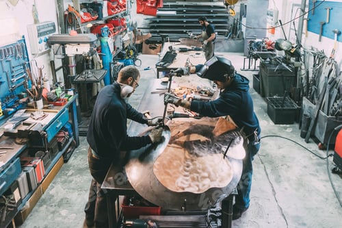Preview: Male metalwork team hammering copper at forge workbench