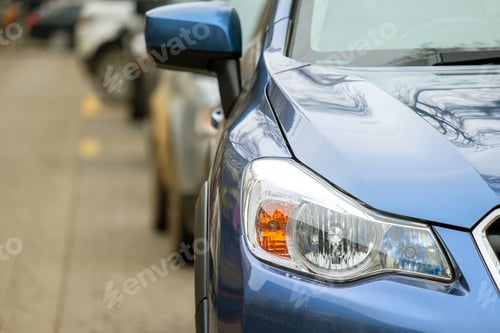 Preview: Closeup of front headlight of new clean car parked on a city street side