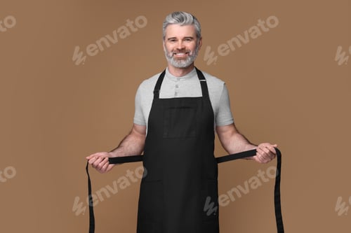 Preview: Happy man wearing kitchen apron on brown background. Mockup for design