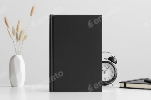 Preview: Black book mockup with a lagurus and workspace accessories on a white table.