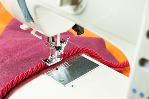 Preview: Modern sewing machine presser foot and decorative edging cord on red fabric. Sewing process.