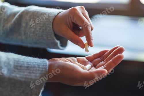 Preview: Closeup image of a woman holding and picking white medicine capsules in hand