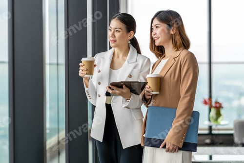 Preview: Two asian businesswomen talking during coffee break in modern office or coworking space