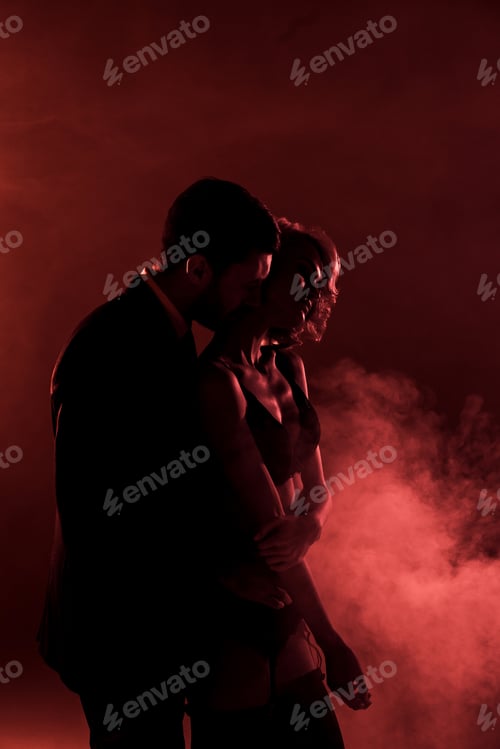 Preview: Man tenderly hugging beautiful woman and kissing her in neck on red smoke background