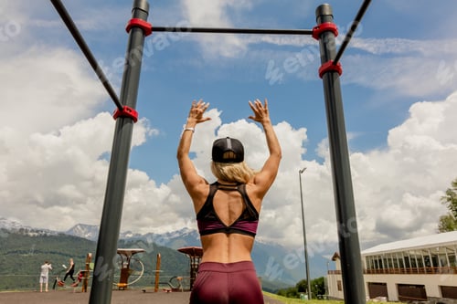 Preview: Athletic woman resting after hard training in the mountains near horizontal bar.