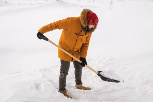 Preview: Young man clearing snow in his backyard village house with shovel. Remove snow from the sidewalk.