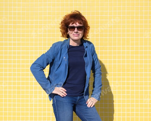 Preview: Confident redhead woman posing with hands on hips against yellow tiled wall