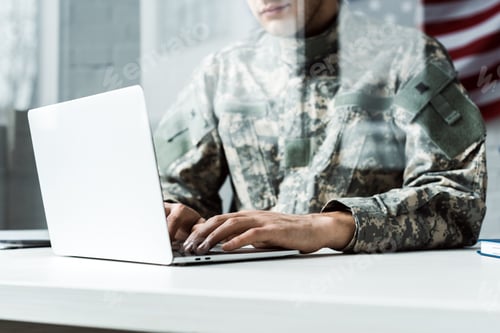 Preview: cropped view of soldier in camouflage uniform using laptop