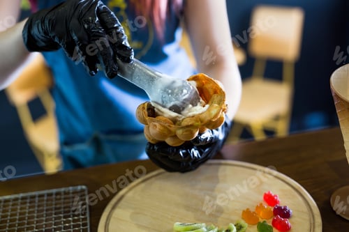 Preview: Cook prepares Hong Kong waffles with ice cream, jam and fruit. Young woman holding Hong Kong bubble