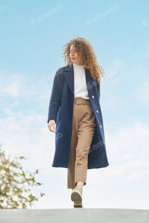 Preview: Cute woman in wool coat walks on the bridge in sunny day