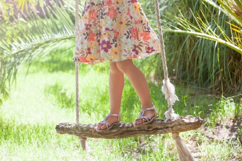 Preview: Waist down cropped shot of girl standing on tree swing in garden