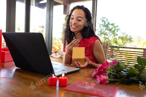 Preview: Biracial young woman with ring video calling through laptop at restaurant