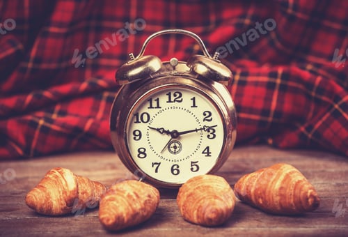 Preview: Retro alarm clock with croissant on a table.