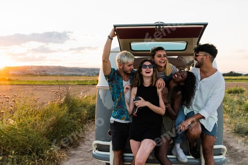 Preview: Group of cheerful young people standing near retro van and laughing while spending time in nature