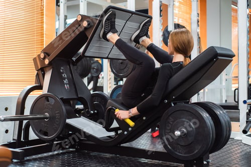 Preview: Young sporty woman does leg exercises on leg press machine