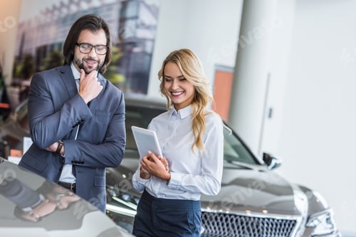 Preview: smiling female auto salon seller with tablet helping businessman to choose car at dealership salon
