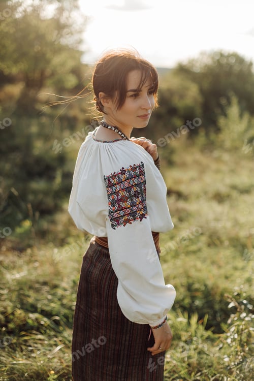 Preview: Young woman in traditional national embroidered shirt and skirt on nature at sunset.