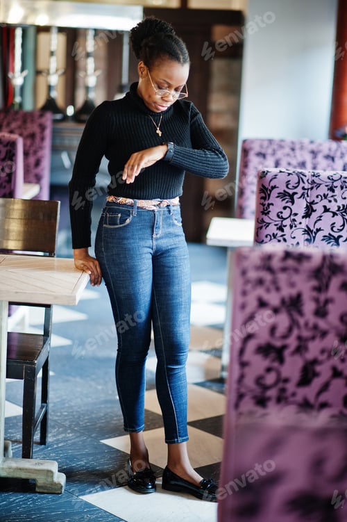 Preview: African woman in black sweater posed at cafe and look at her smart watches.