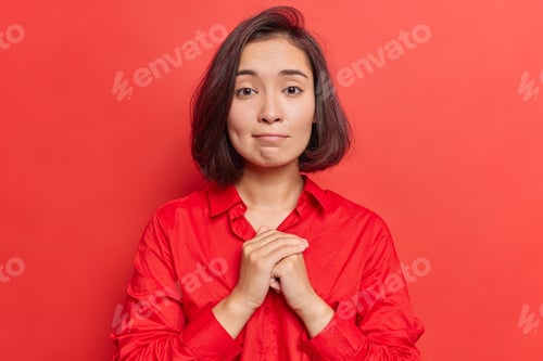 Preview: Hopeful good looking young Asian woman keeps hands together in pray gesture has pity expression asks