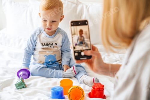 Preview: Mother taking photo of her blonde baby son on mobile phone