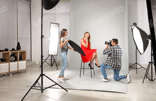 Preview: Professional photographer with assistant taking picture of young woman in modern studio