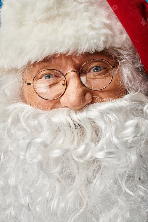 Preview: close up of happy Santa Claus with white beard and eyeglasses looking at camera on blue background