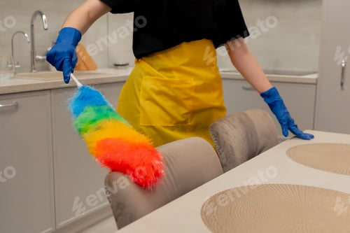 Preview: close up in the apartment cleaning lady in a yellow apron is cleaning chairs with a dust brush