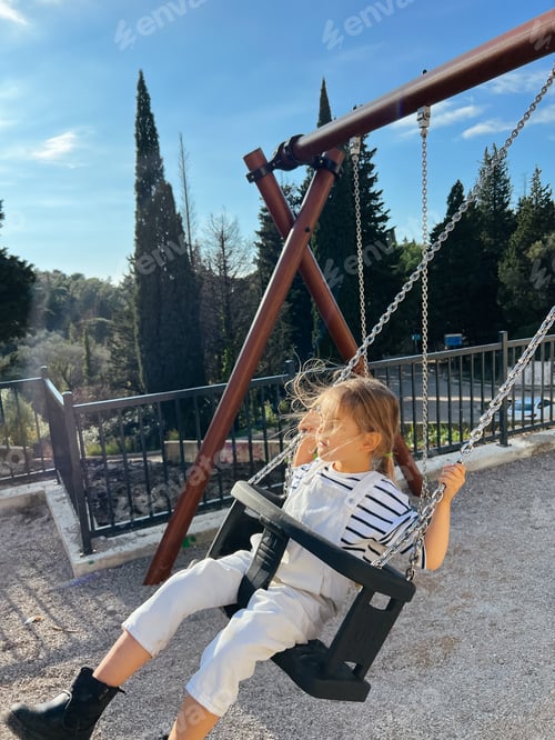 Preview: Little girl swings on a chain swing in the park with her eyes closed