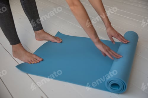 Preview: Woman Rolling Out Yoga Mat on Wooden Floor
