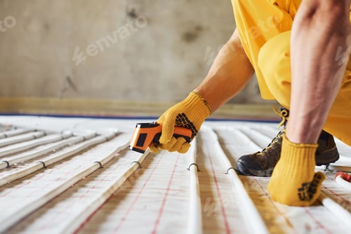 Preview: Measures heat of the pipes. Worker in yellow colored uniform installing underfloor heating system