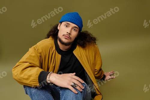 Preview: Handsome young man with a beard and blue beanie showcasing casual streetwear style in studio light