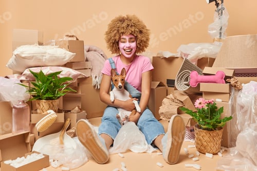 Preview: Happy young woman rests seated on floor with favorite pet daydreams about bright future in new first