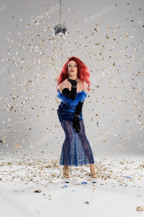 Preview: Elegant drag queen in dress and gloves blowing air kiss under disco ball and confetti on grey