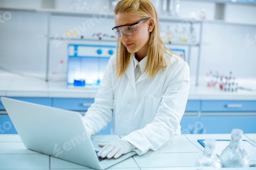 Preview: Female researcher in white lab coat and protective goggles