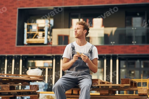 Preview: Eating food. Young man working in uniform at construction at daytime
