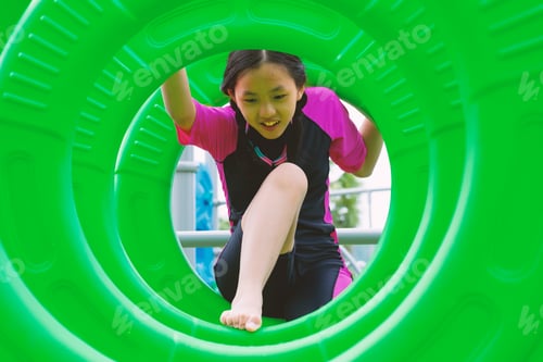 Preview: Full body portrait of a Thai girl in casual outfit climbing green hanging tunnel in a fun park on