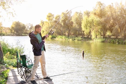 Preview: Man with rod fishing on wooden pier at riverside. Recreational activity