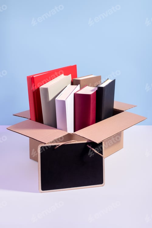 Preview: Books in a box ready for donation on blue with empty sign for text, copy space.