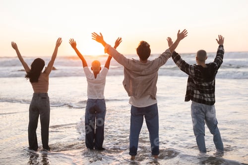 Preview: Friends raising arms at beach during golden hour sunset