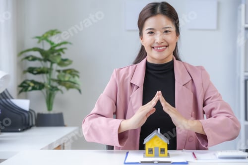 Preview: Smiling real estate agent protecting house model with hands