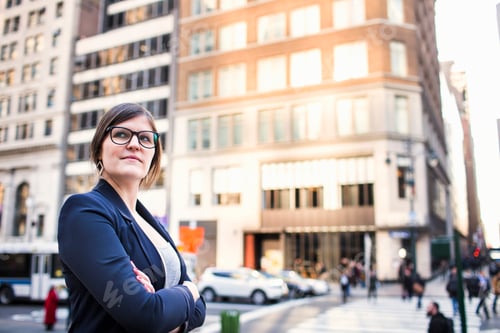 Preview: Confident businesswoman with arms crossed standing against buildings in city