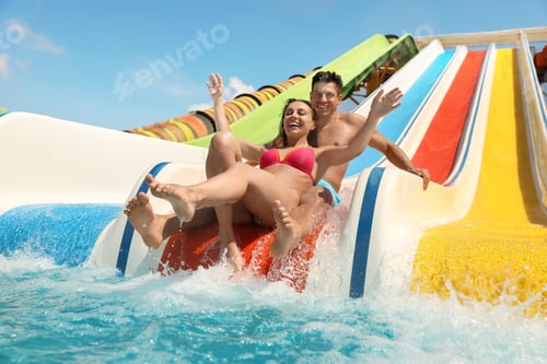 Preview: Happy couple on slide at water park, low angle view. Summer vacation